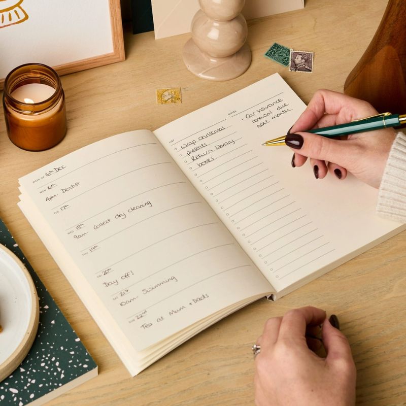 Mains écrivant le planning hebdomadaire dans l'agenda perpétuel Palmier Ink & Bloom format A5