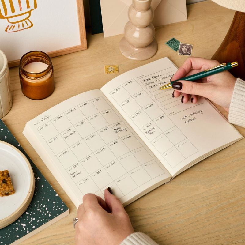 Mains remplissant la vue mensuelle de l'agenda perpétuel Palmier Ink & Bloom - juillet