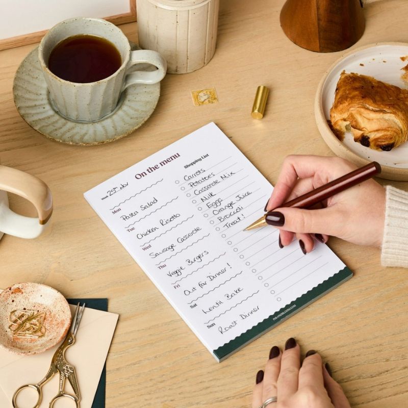 Meal Planner On the Menu Ink & Bloom rempli à la main sur un bureau avec thé et croissant - planificateur repas A5 avec liste de courses