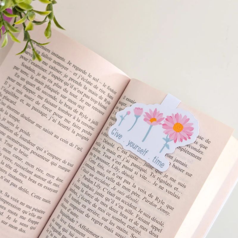 Marque-page magnétique Give Yourself Time clipsé sur les pages d'un livre ouvert, illustration marguerites roses