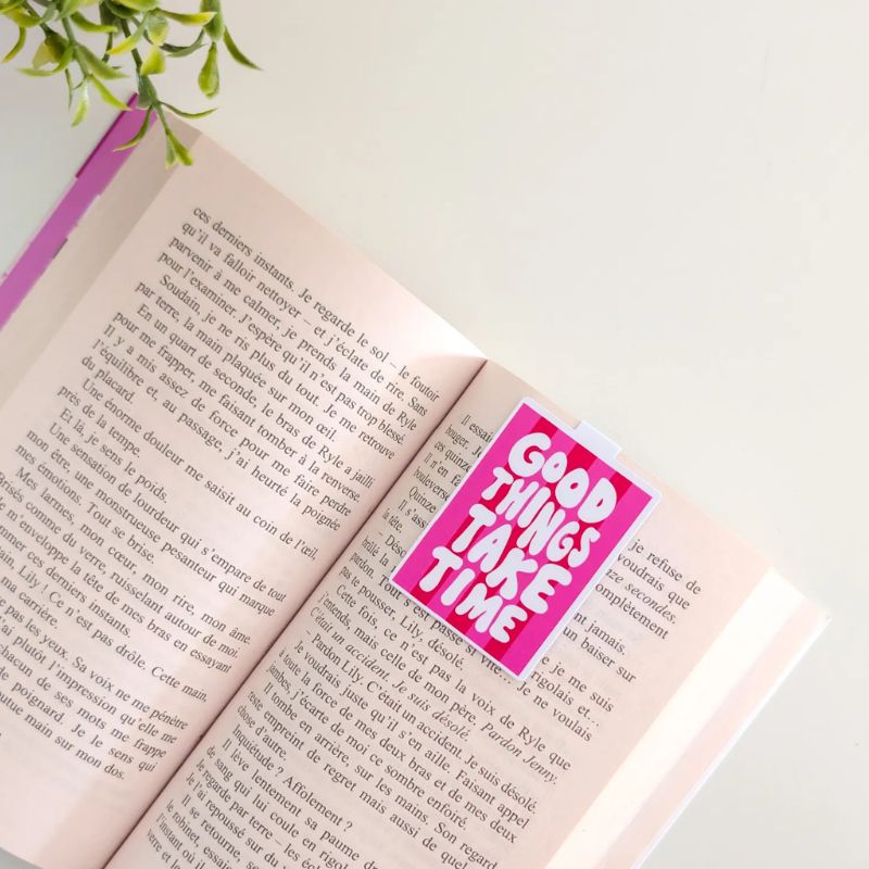 Marque-page magnétique Good Things Take Time clipsé sur les pages d'un livre ouvert, design pop rose et rouge