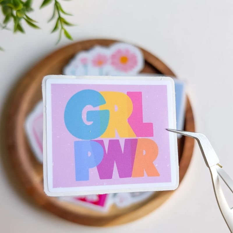 Sticker Girl Power décollé de sa planche avec une pince, lettering coloré sur fond lilas