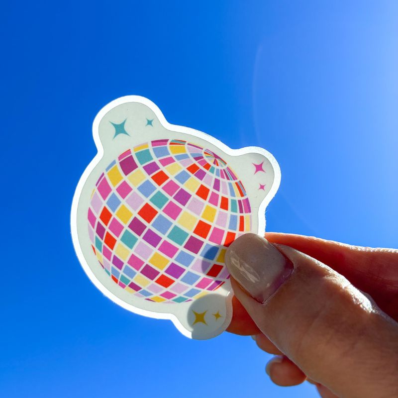 Sticker Disco Ball tenu à la main devant un ciel bleu, illustration boule à facettes colorée